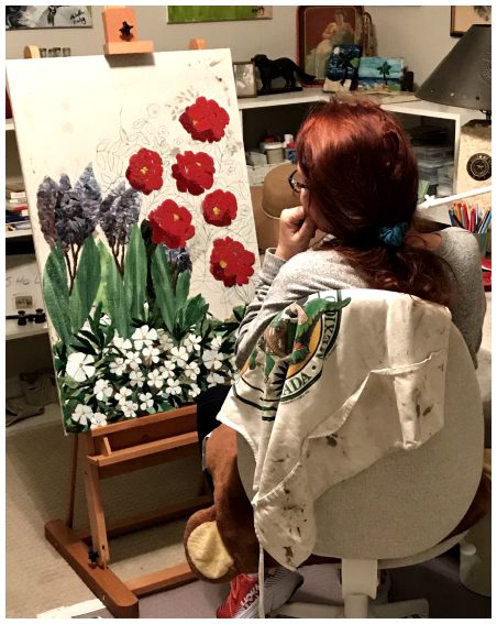 A woman sitting in front of an easel painting flowers.