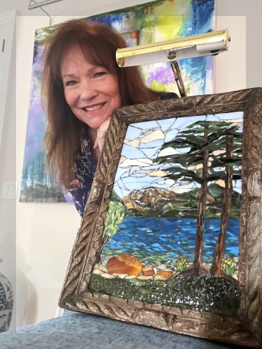 A woman holding up a picture of trees and water.